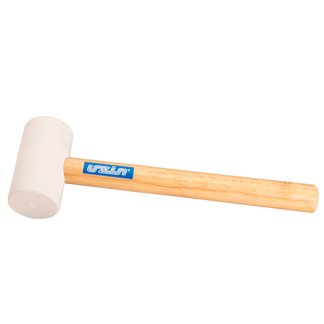 UZIN_Dummy_rubber hammer-UZIN_2014-11 Photo produit en gros plan d'un maillet en caoutchouc : tête en caoutchouc beige clair fixée à un manche en bois clair et lisse avec une étiquette de marque rectangulaire bleue ; l'outil est placé en diagonale sur un fond blanc uni, éclairé doucement pour faire ressortir la texture du caoutchouc et le fil du bois ; adapté pour des frappes délicates en menuiserie, montage ou pose de carrelage.