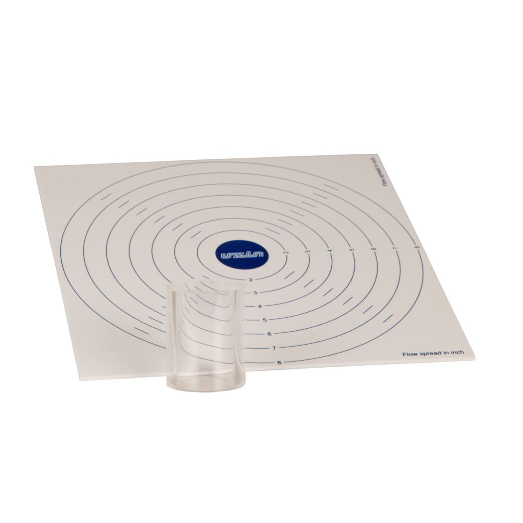 UZIN_Dummy_flow spread disc-inch_2017-09 Un tapis de mesure carré blanc incliné avec des marques circulaires concentriques en bleu, un petit gobelet en plastique transparent placé près du bas au centre et un logo bleu au centre ; les anneaux sont numérotés et la mention 'Flow spread in inch' est visible en bas à droite.